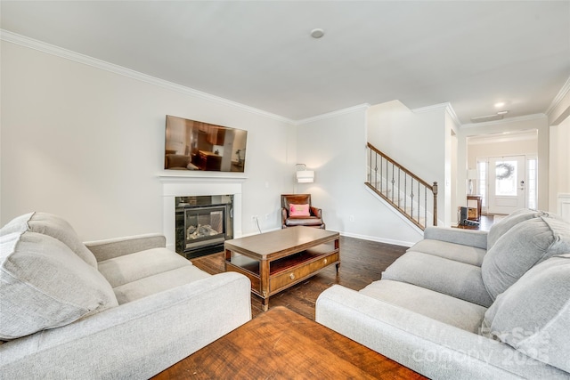 living area with dark wood-style floors, stairs, crown molding, and a glass covered fireplace