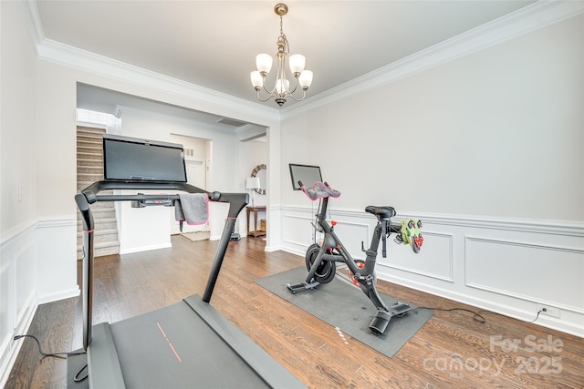 workout area featuring a wainscoted wall, crown molding, wood finished floors, and an inviting chandelier