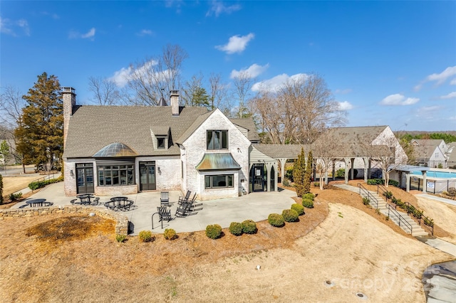 rear view of property with a shingled roof, a chimney, and a patio area