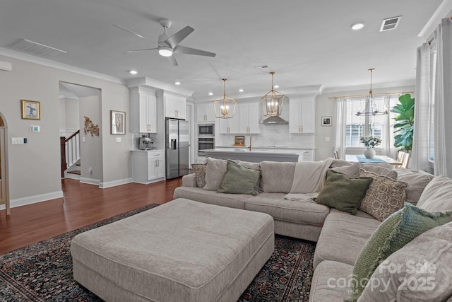 living room with dark wood-type flooring, visible vents, baseboards, stairs, and crown molding