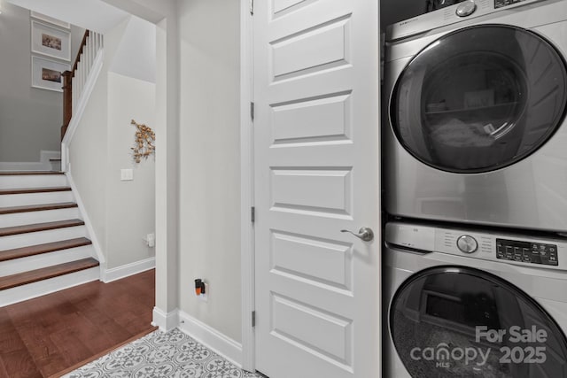 clothes washing area with stacked washer / dryer, laundry area, baseboards, and wood finished floors