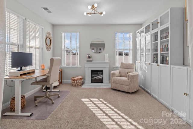 office featuring carpet, a notable chandelier, visible vents, a glass covered fireplace, and baseboards