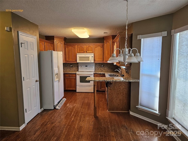 kitchen featuring dark wood-style flooring, brown cabinetry, a sink, white appliances, and a peninsula