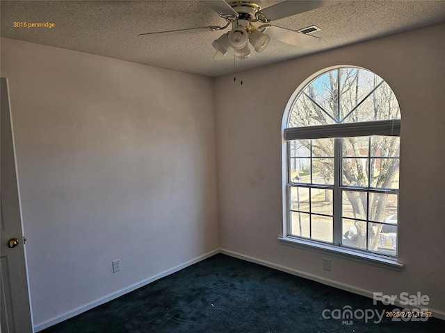 empty room with a textured ceiling, dark colored carpet, plenty of natural light, and visible vents