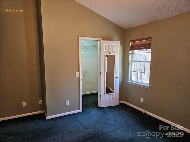 unfurnished bedroom featuring lofted ceiling, baseboards, a spacious closet, a closet, and dark colored carpet