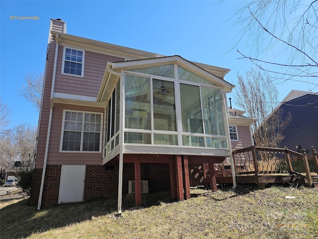 back of house featuring a sunroom, a chimney, central AC unit, and brick siding