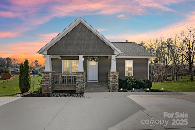 craftsman-style house featuring covered porch, a front lawn, and roof with shingles