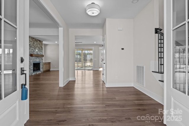 entryway with a stone fireplace, dark wood finished floors, visible vents, and baseboards