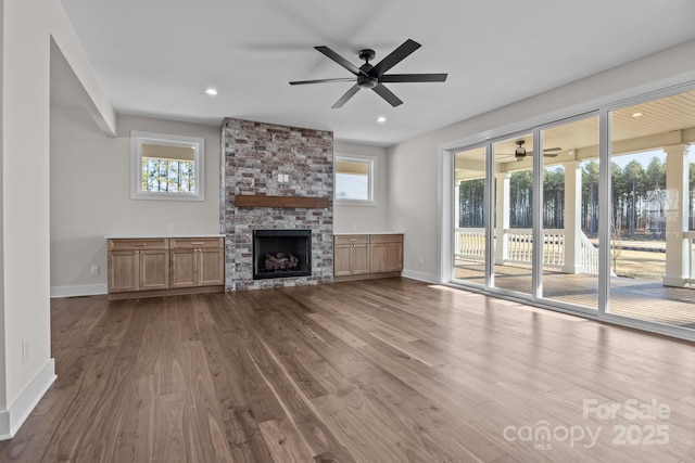 unfurnished living room with recessed lighting, baseboards, wood finished floors, and a stone fireplace