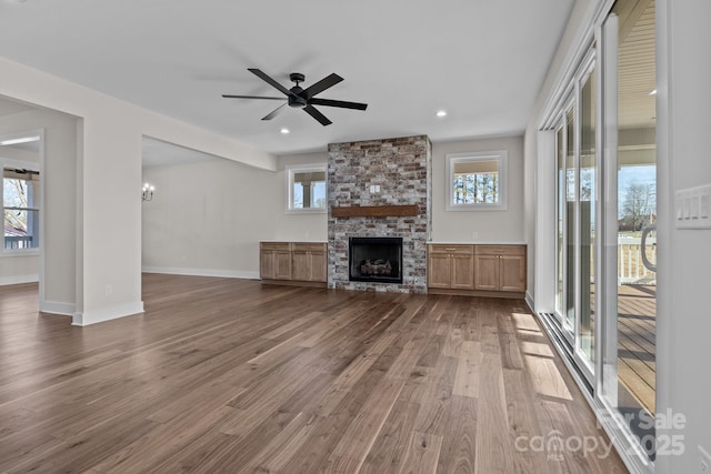 unfurnished living room with recessed lighting, dark wood-type flooring, a ceiling fan, a stone fireplace, and baseboards