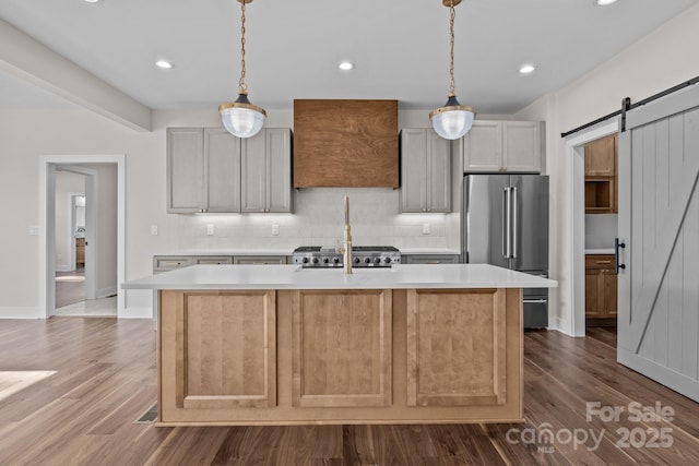 kitchen featuring a center island with sink, high end fridge, light countertops, backsplash, and a barn door