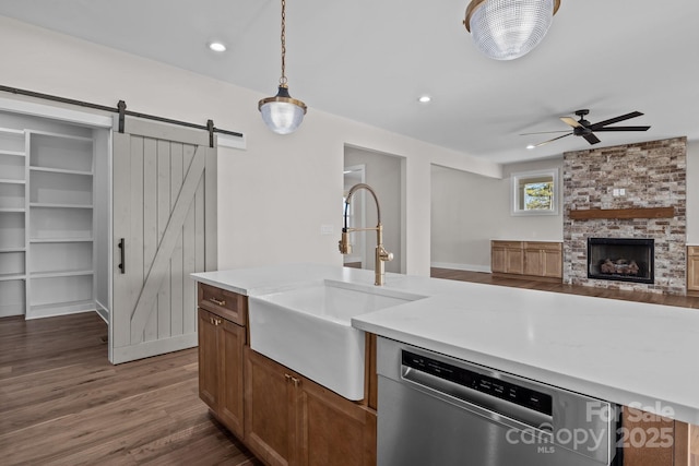 kitchen featuring a barn door, a sink, light countertops, stainless steel dishwasher, and pendant lighting