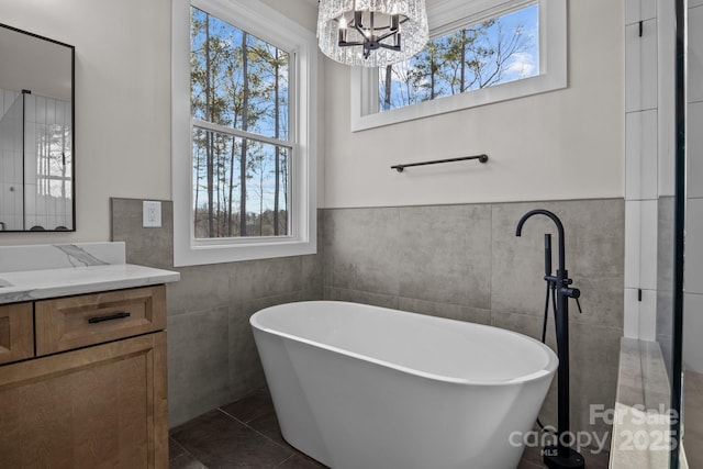 bathroom with a freestanding tub, tile walls, an inviting chandelier, and vanity