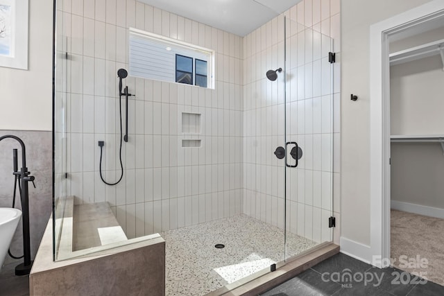 full bathroom with a spacious closet, a stall shower, a soaking tub, and baseboards