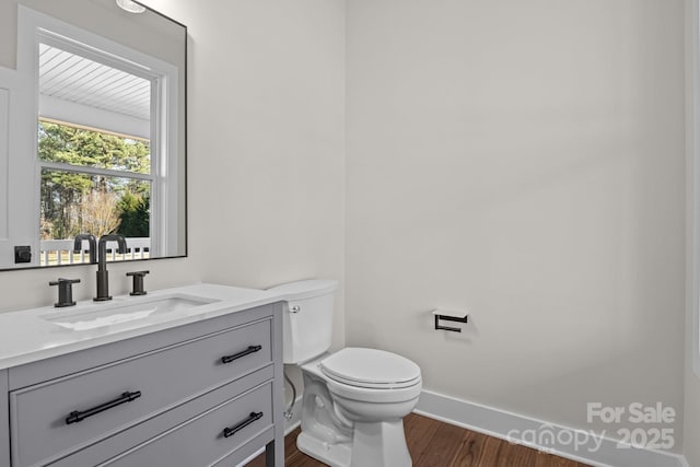 bathroom featuring toilet, baseboards, wood finished floors, and vanity