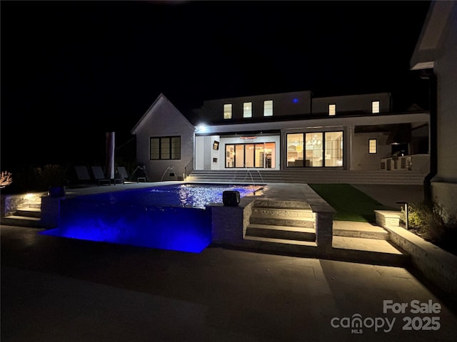 pool at night with a patio and an outdoor pool