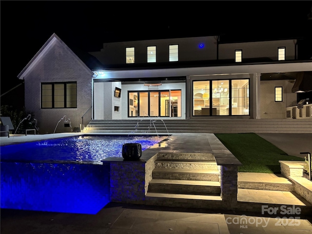 back of house at night with an outdoor pool