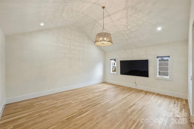 unfurnished living room with lofted ceiling, a notable chandelier, light wood-style flooring, and baseboards