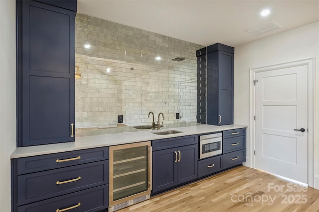 bar featuring wine cooler, light wood finished floors, visible vents, decorative backsplash, and a sink