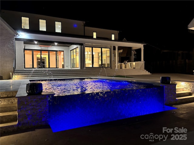 pool at night featuring entry steps and an outdoor pool