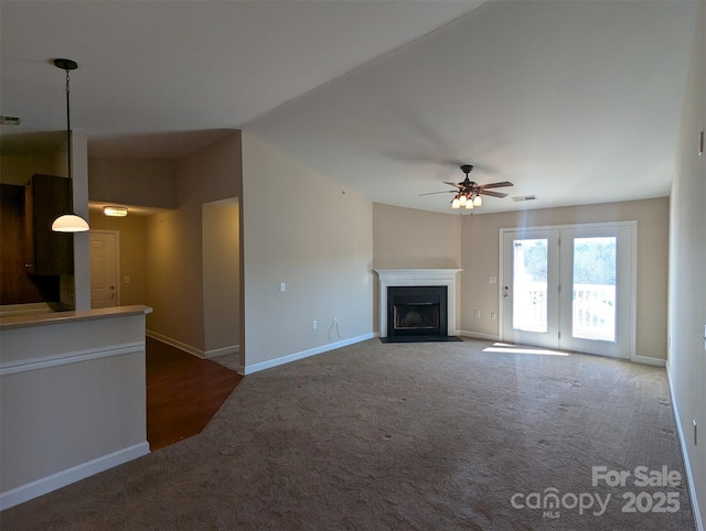 unfurnished living room featuring baseboards, visible vents, a ceiling fan, a fireplace with flush hearth, and dark colored carpet