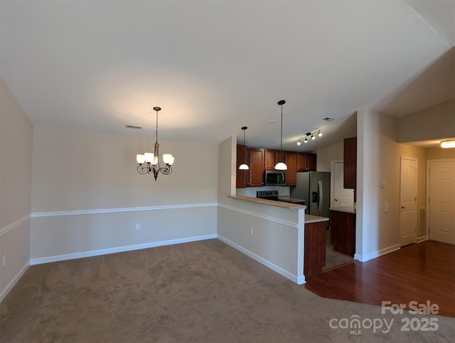 kitchen featuring a peninsula, light countertops, appliances with stainless steel finishes, brown cabinetry, and pendant lighting