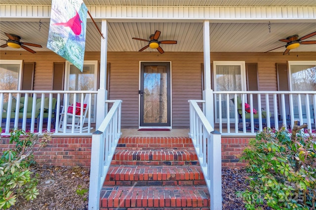 view of exterior entry featuring covered porch, a ceiling fan, and brick siding