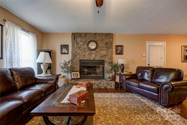 living room featuring a textured ceiling, wood finished floors, and a stone fireplace