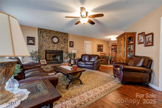 living room featuring dark wood-style floors, a fireplace, a textured ceiling, and a ceiling fan