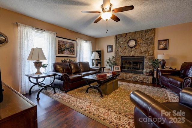 living area with a ceiling fan, a fireplace, a textured ceiling, and wood finished floors