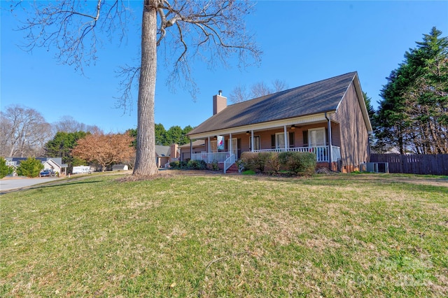 view of front facade with covered porch, a chimney, fence, and a front lawn