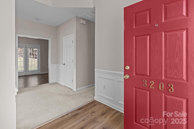 carpeted entryway featuring french doors, a wainscoted wall, a decorative wall, and wood finished floors