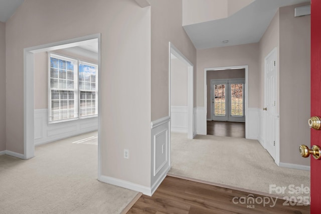 hallway with wood finished floors, wainscoting, carpet flooring, and a decorative wall