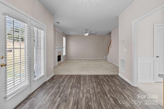 unfurnished room with ceiling fan, a fireplace, wood finished floors, visible vents, and stairway