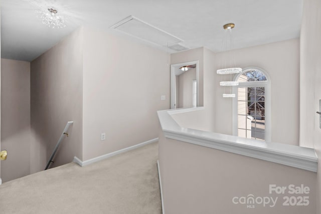 hallway featuring attic access, baseboards, carpet flooring, and an upstairs landing