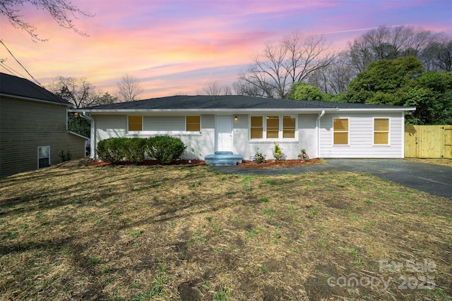 ranch-style home featuring aphalt driveway, brick siding, and fence