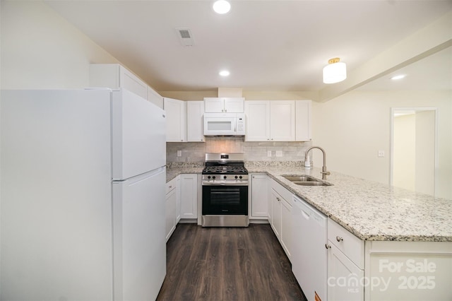 kitchen featuring visible vents, backsplash, a sink, white appliances, and a peninsula