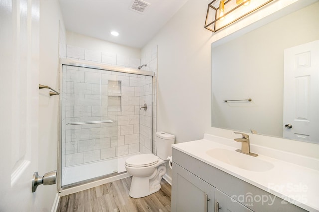 bathroom featuring visible vents, toilet, a tile shower, vanity, and wood finished floors