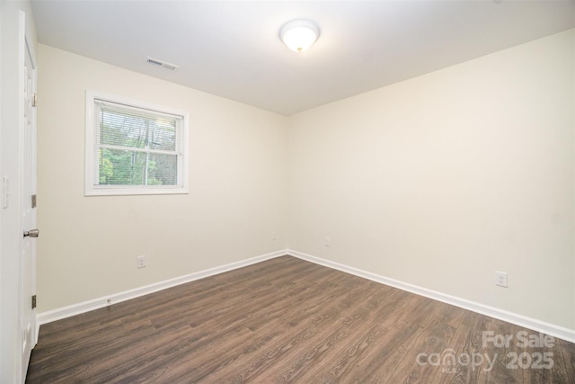 spare room featuring dark wood-type flooring, visible vents, and baseboards