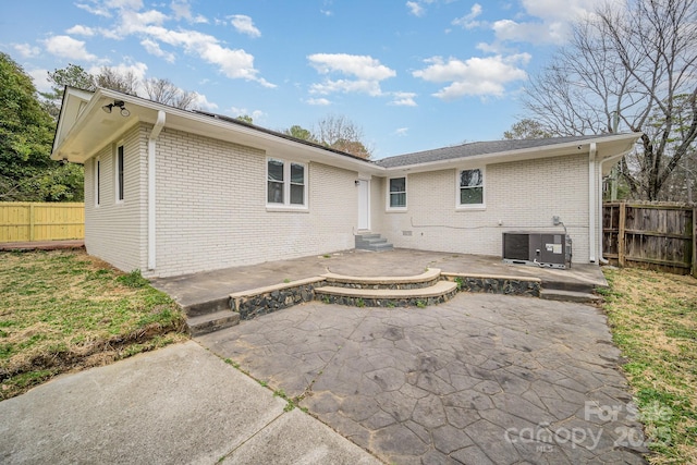 back of property with central air condition unit, a patio area, fence, and brick siding