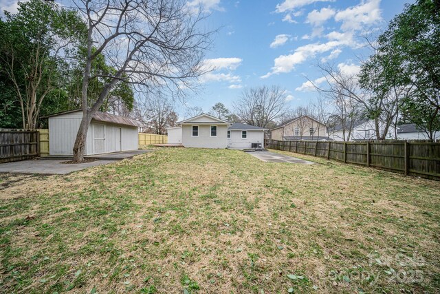 rear view of property featuring a yard, a storage unit, a patio area, a fenced backyard, and an outdoor structure