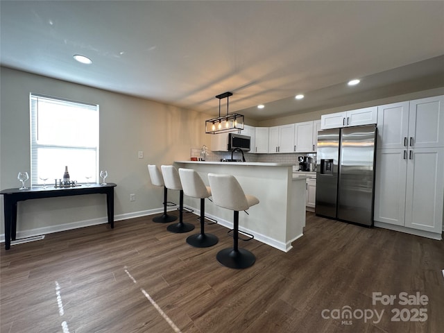 kitchen with dark wood-style floors, appliances with stainless steel finishes, a breakfast bar, a peninsula, and backsplash