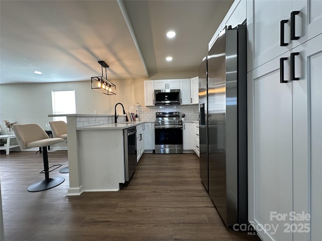 kitchen with stainless steel appliances, a peninsula, dark wood-style flooring, a sink, and backsplash