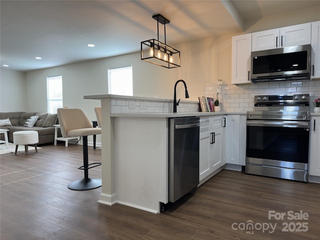 kitchen featuring tasteful backsplash, appliances with stainless steel finishes, dark wood-type flooring, white cabinets, and a peninsula