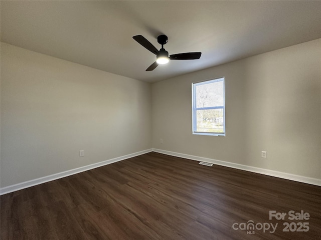 empty room with dark wood-style floors, visible vents, baseboards, and a ceiling fan