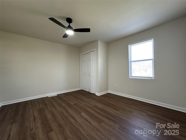 unfurnished bedroom featuring dark wood-style floors, a closet, baseboards, and a ceiling fan