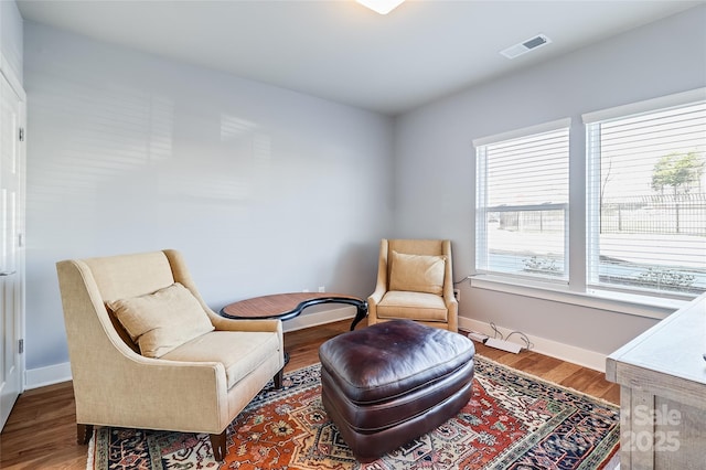 sitting room with wood finished floors, visible vents, and baseboards