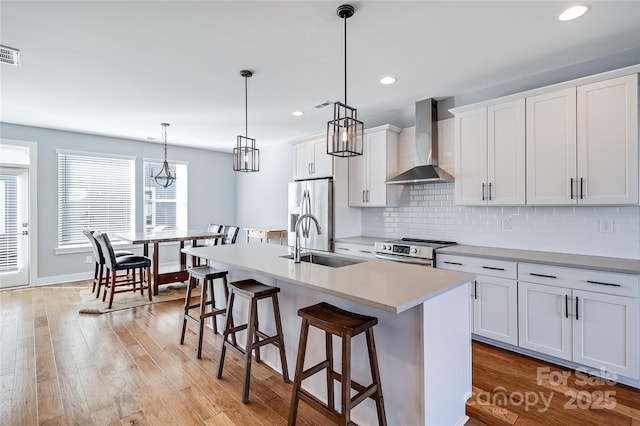 kitchen with light wood-style floors, stainless steel appliances, wall chimney range hood, a kitchen bar, and a sink