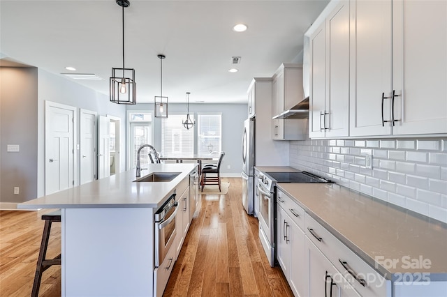 kitchen with stainless steel appliances, tasteful backsplash, light wood-style floors, a kitchen island with sink, and a sink