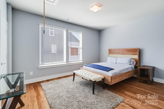 bedroom with light wood finished floors, attic access, visible vents, and baseboards